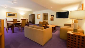 A hotel room with a purple carpet, beige sofas, a wooden dining table, and a TV mounted on the wall.