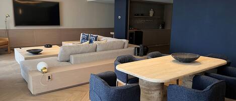 Un salon moderne avec un canapé, une table à manger et des chaises. Un téléviseur à écran plat est fixé au mur, ainsi qu’une table basse et une bibliothèque.