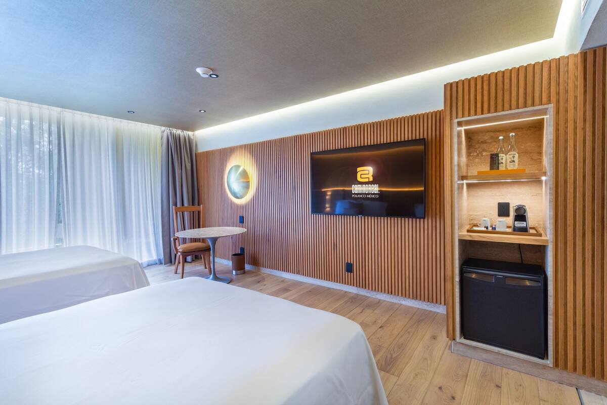 A hotel room with two beds, a TV, a small table, and a built-in mini-fridge.