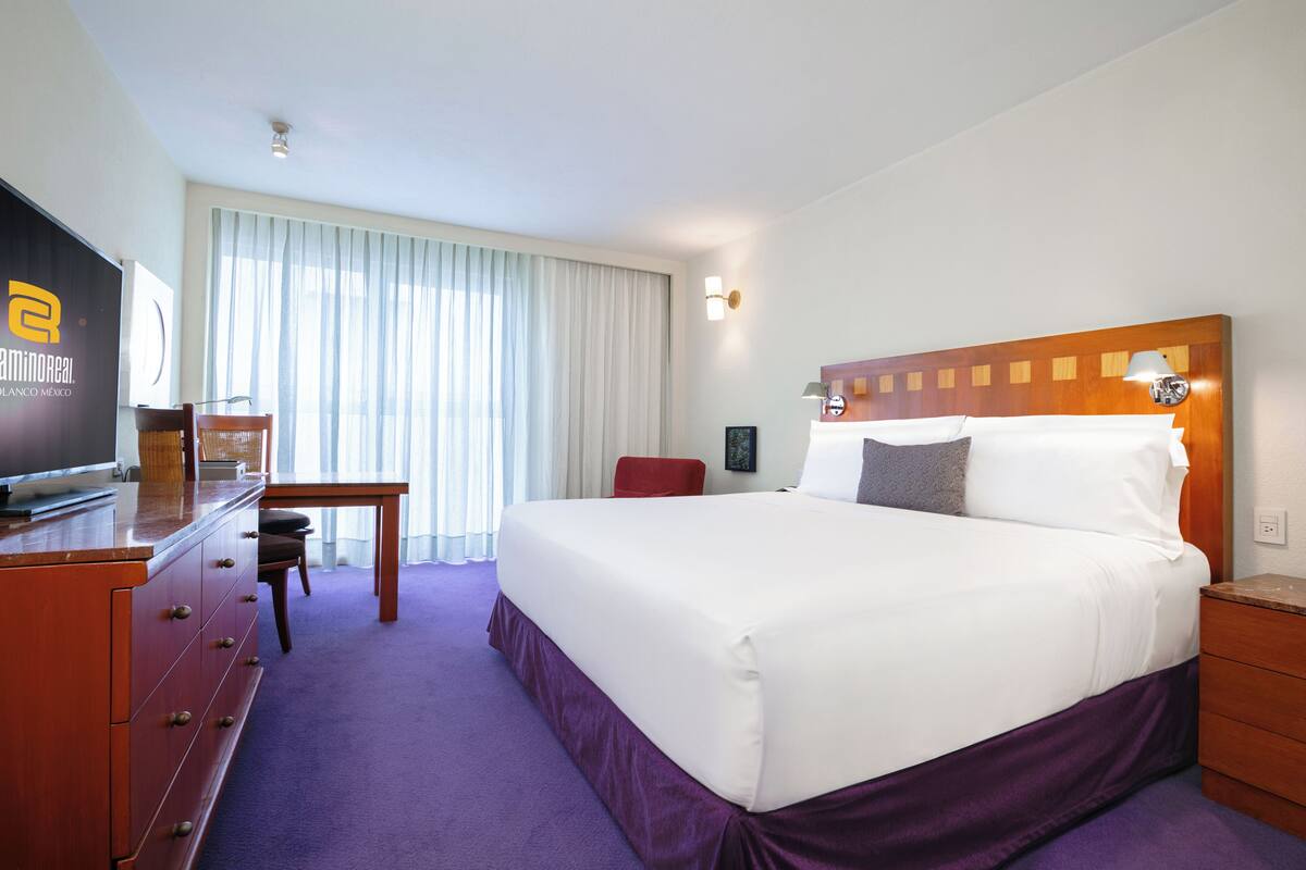 A hotel room with a large bed, a wooden dresser, a desk, and a television.