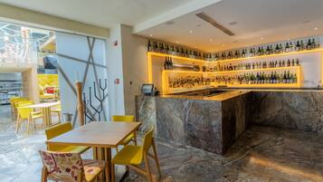 A bar area with a marble counter, yellow chairs, and a variety of bottles.
