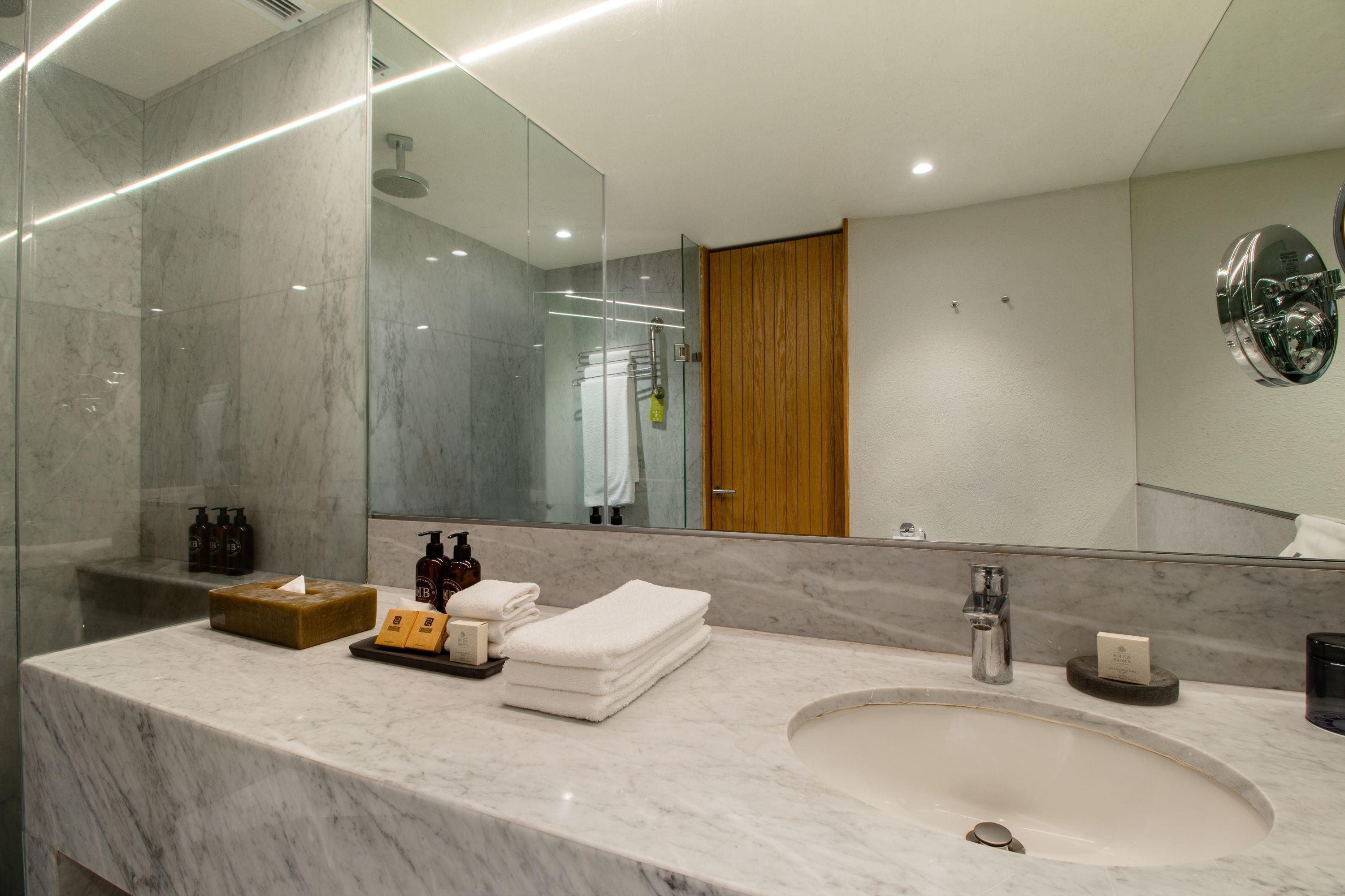 A modern bathroom with a marble sink, a large mirror, and a glass-enclosed shower.