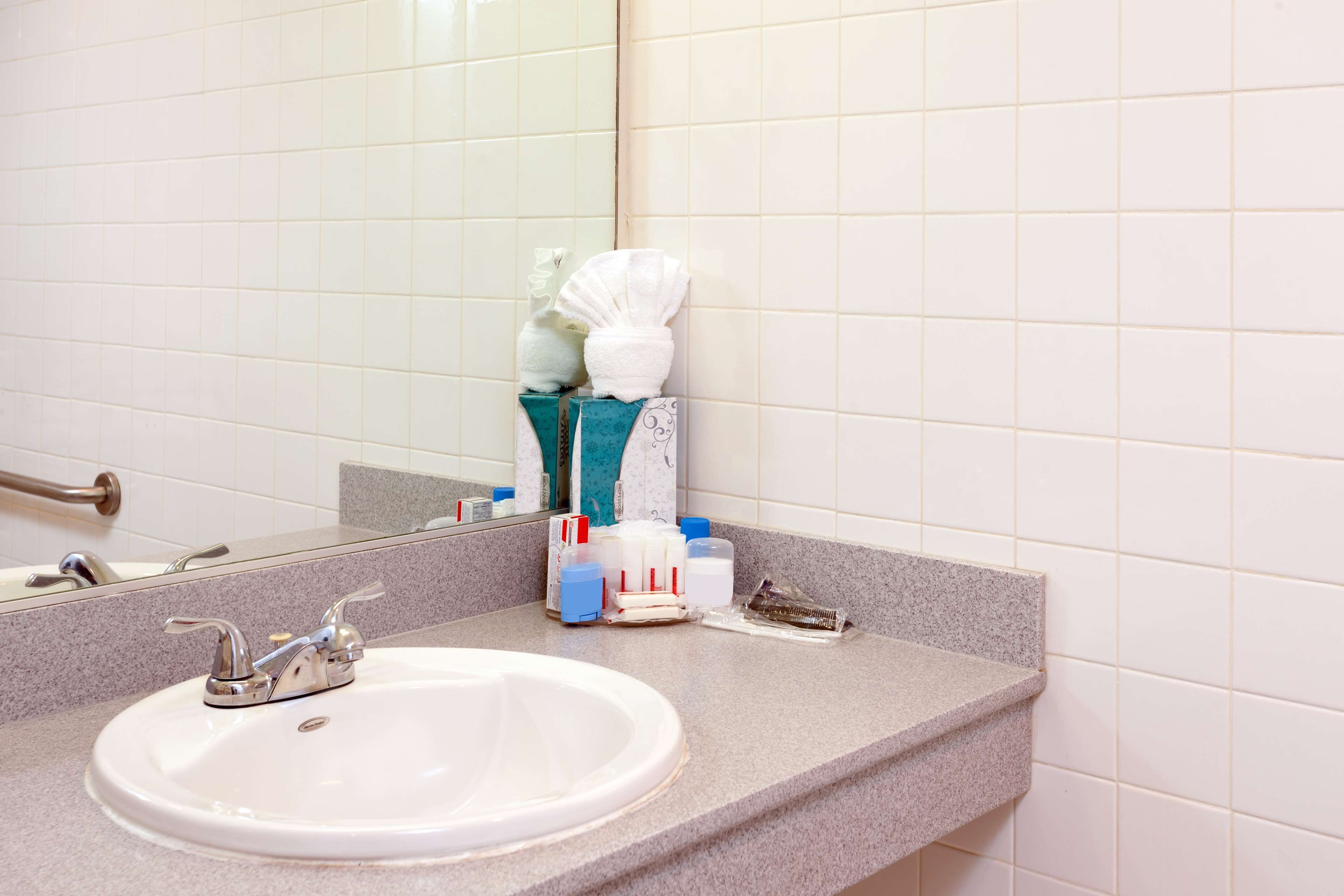 A bathroom with a white sink, a mirror, and toiletries on the countertop.