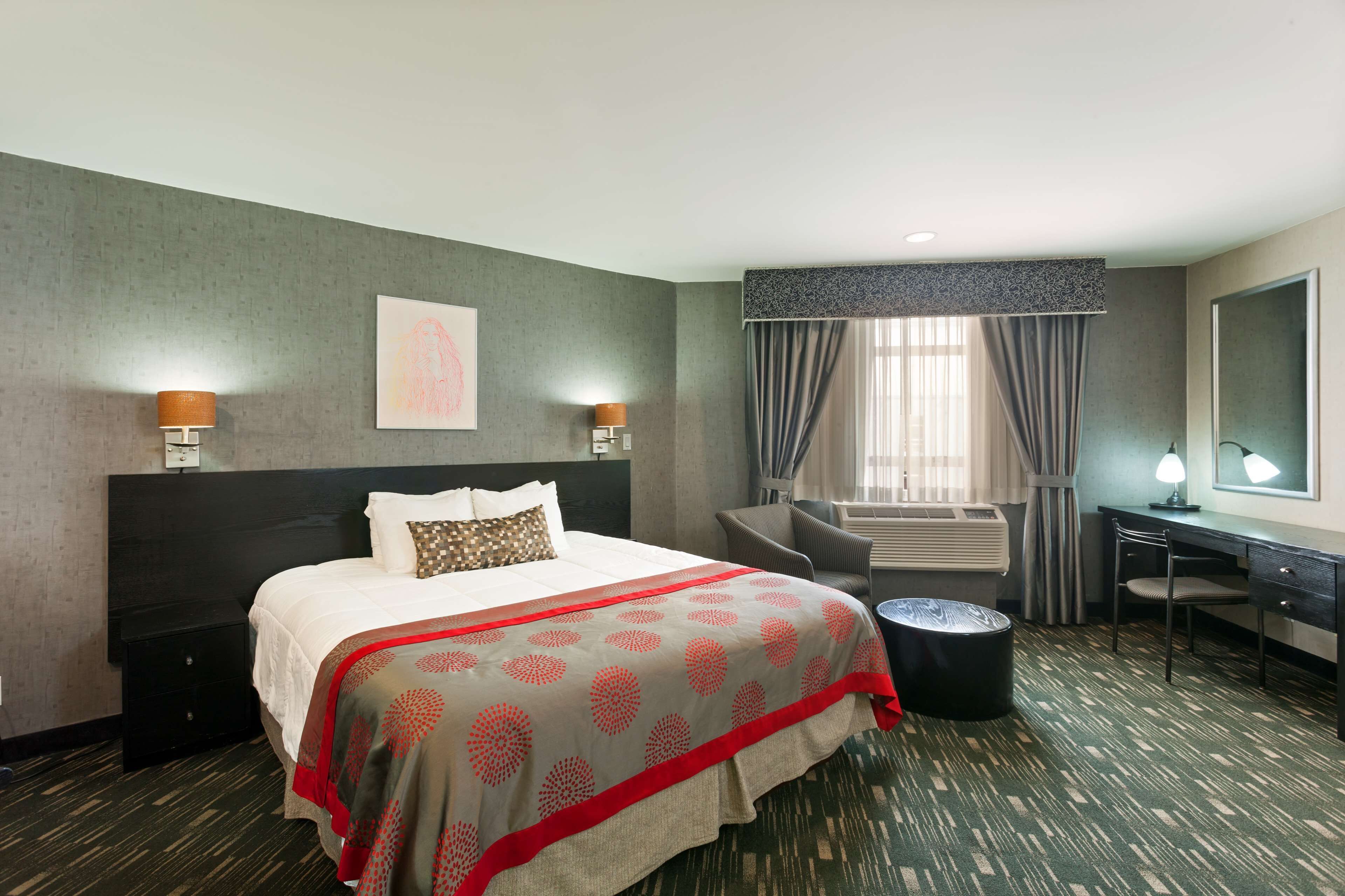 Une chambre d’hôtel avec un grand lit, un bureau, une chaise, une petite table et une fenêtre avec des rideaux.