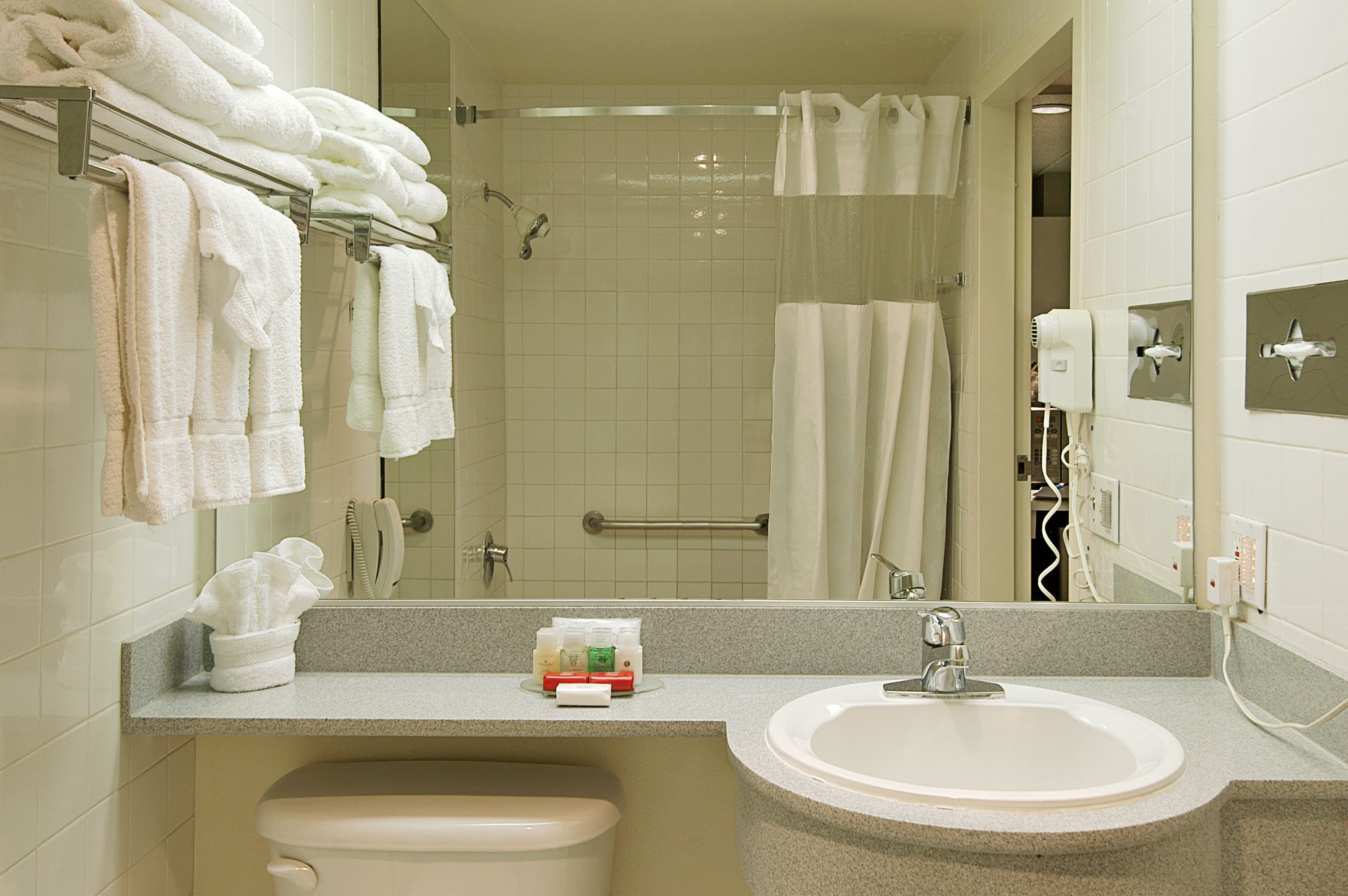 Un baño con lavabo, espejo, toallero, ducha y secador de pelo.