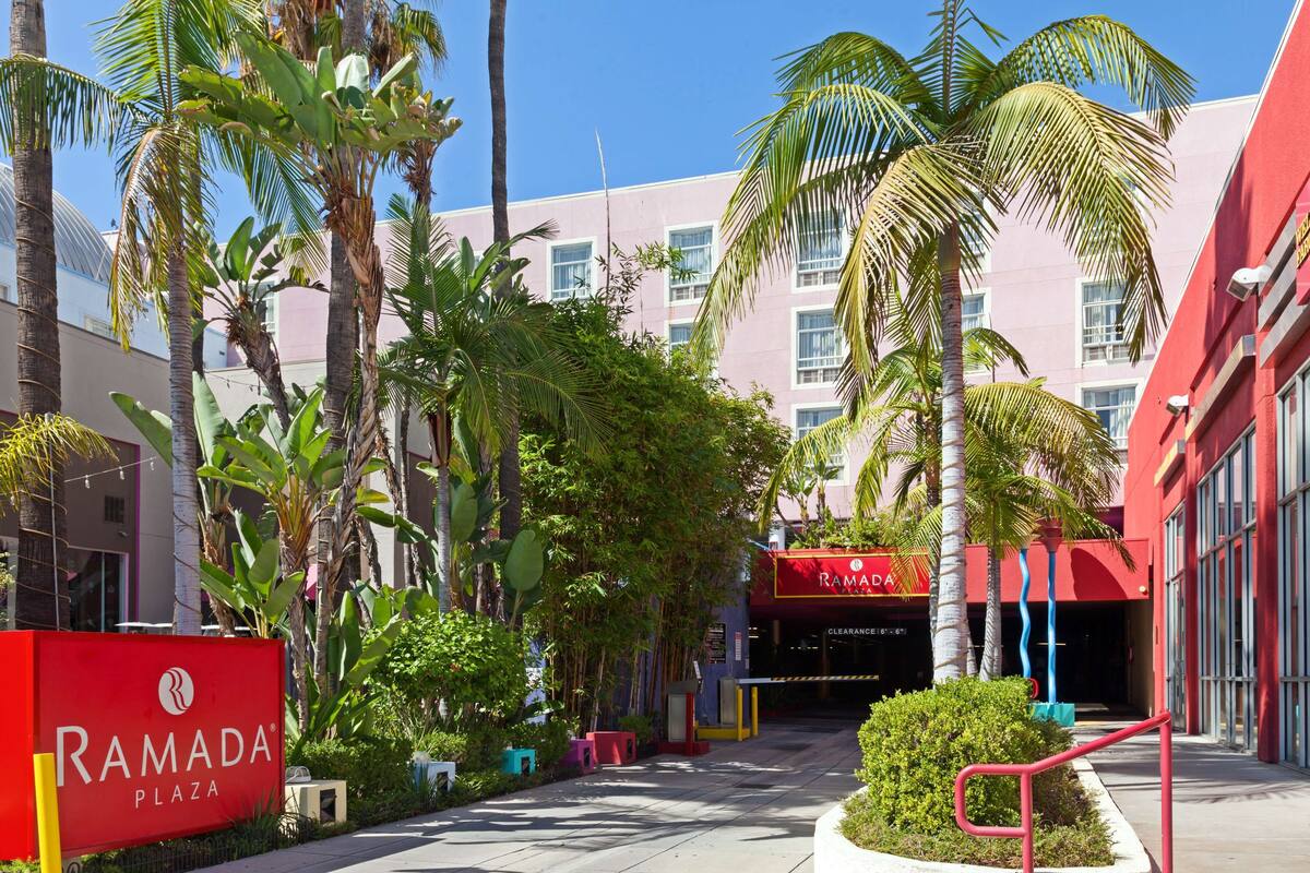 A hotel entrance with a red sign, palm trees, and a clear sky.