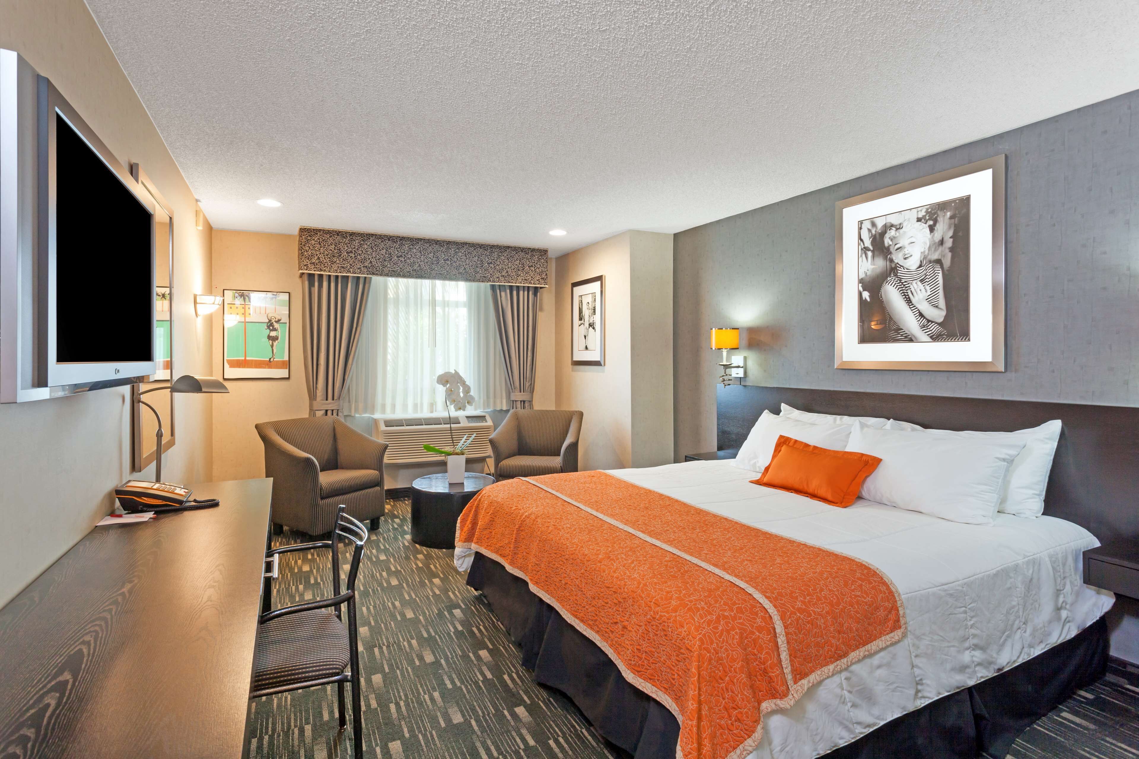 A hotel room with a large bed, a desk, a chair, a TV, and a window with curtains.