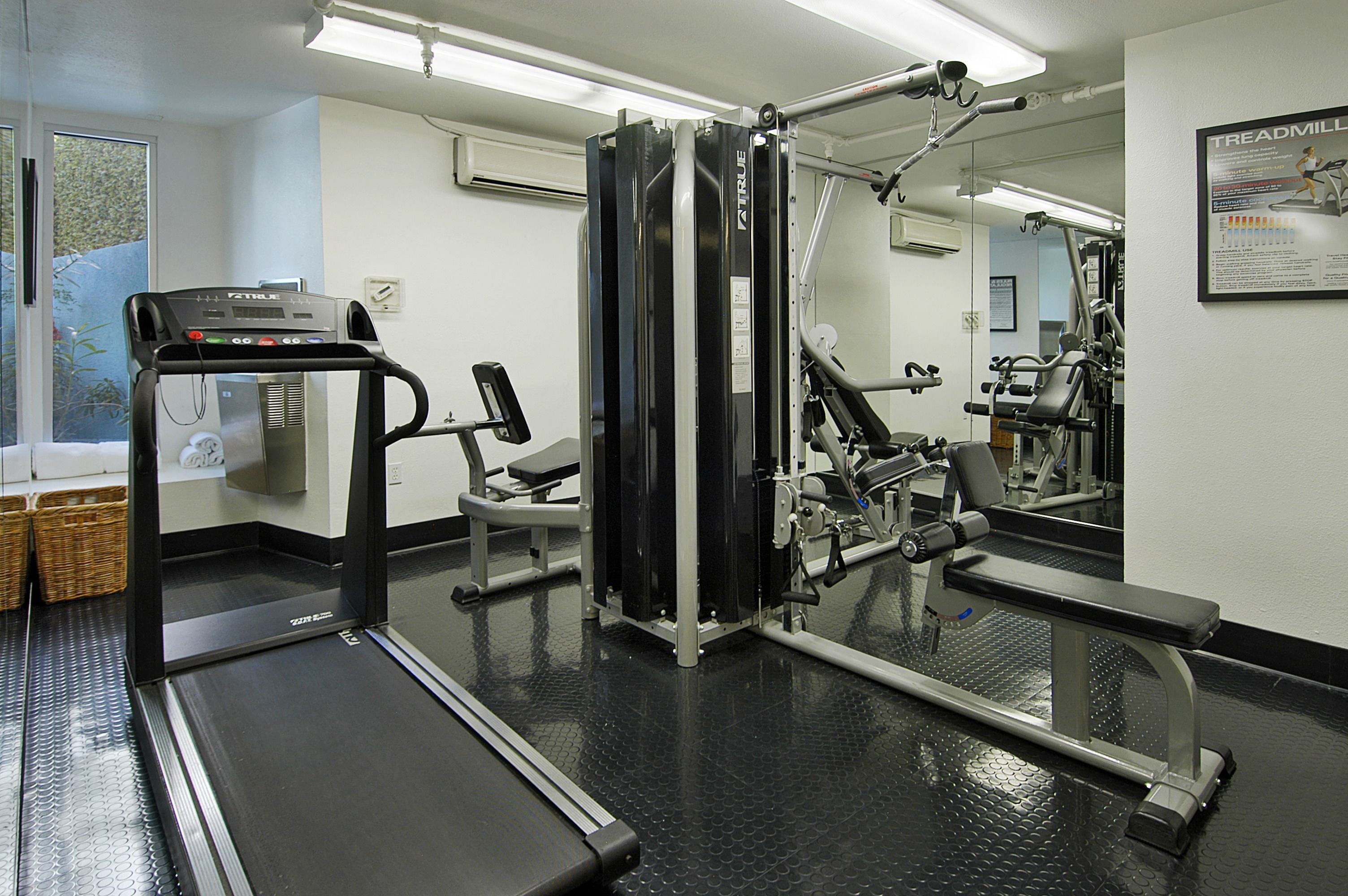 Una palestra con macchinari cardio, panche per pesi e uno specchio a parete.