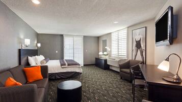 A hotel room with a bed, sofa, desk, and TV.