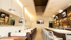 A modern restaurant interior with a long counter, bar area, and seating along the walls. - Ramada Plaza by Wyndham West Hollywood Hotel & Suites (West Hollywood)