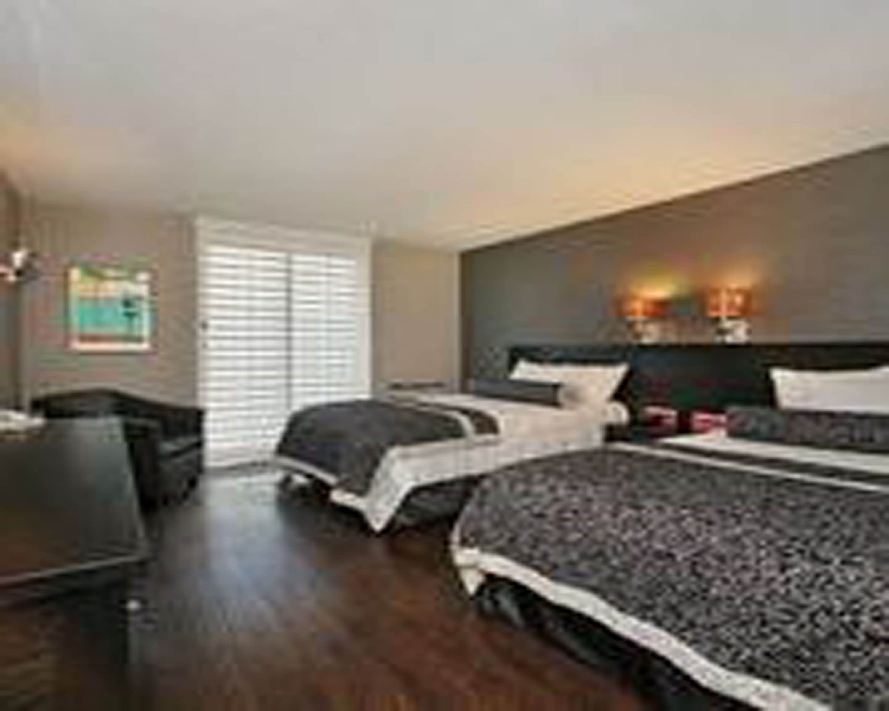 A hotel room with a large bed, a desk, and a window with blinds.