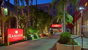 A well-lit plaza with a prominent 'Ramada Plaza' sign, surrounded by palm trees and a building with large windows. - Ramada Plaza by Wyndham West Hollywood Hotel & Suites (West Hollywood)