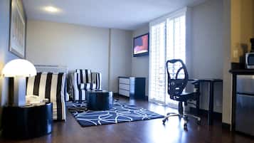 Een moderne woonkamer met een donker houten vloer, gestreepte banken, een zwarte bureaustoel, een flatscreen televisie en een groot raam met jaloezieën.