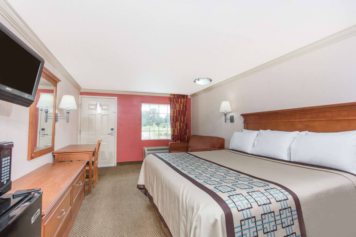 A hotel room with a bed, a desk, a television, and a window with curtains.