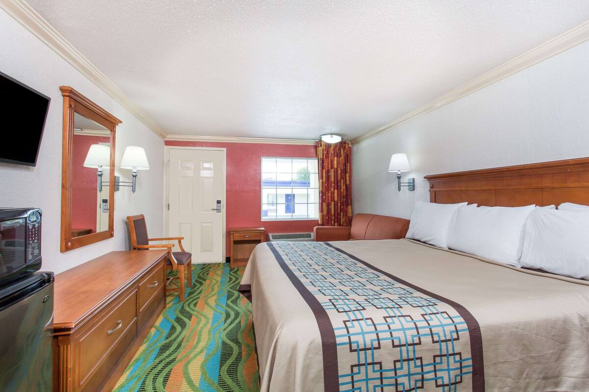 A hotel room with a bed, dresser, television, and a window with curtains.