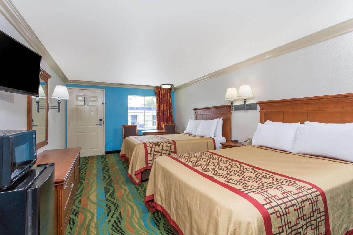 A hotel room with two beds, a TV, a desk with a microwave, and a window with curtains.
