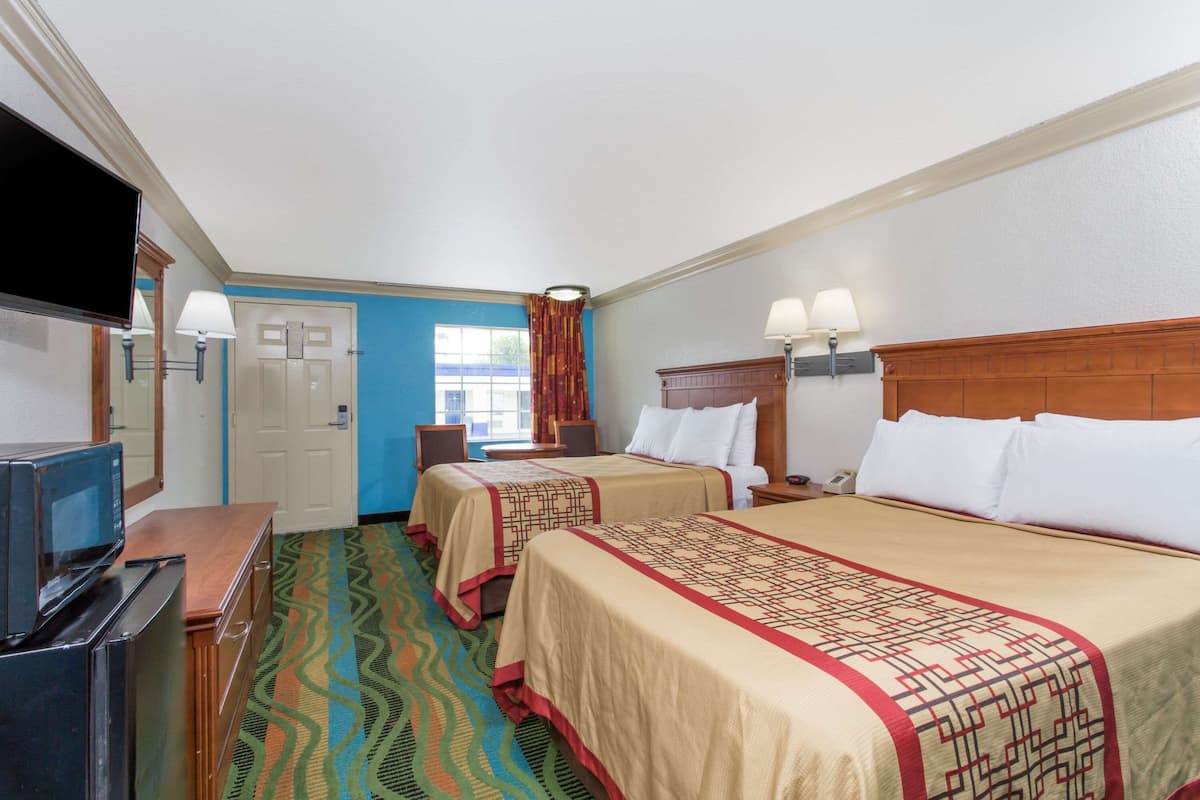 A hotel room with two beds, a TV, a desk, and a window with curtains.