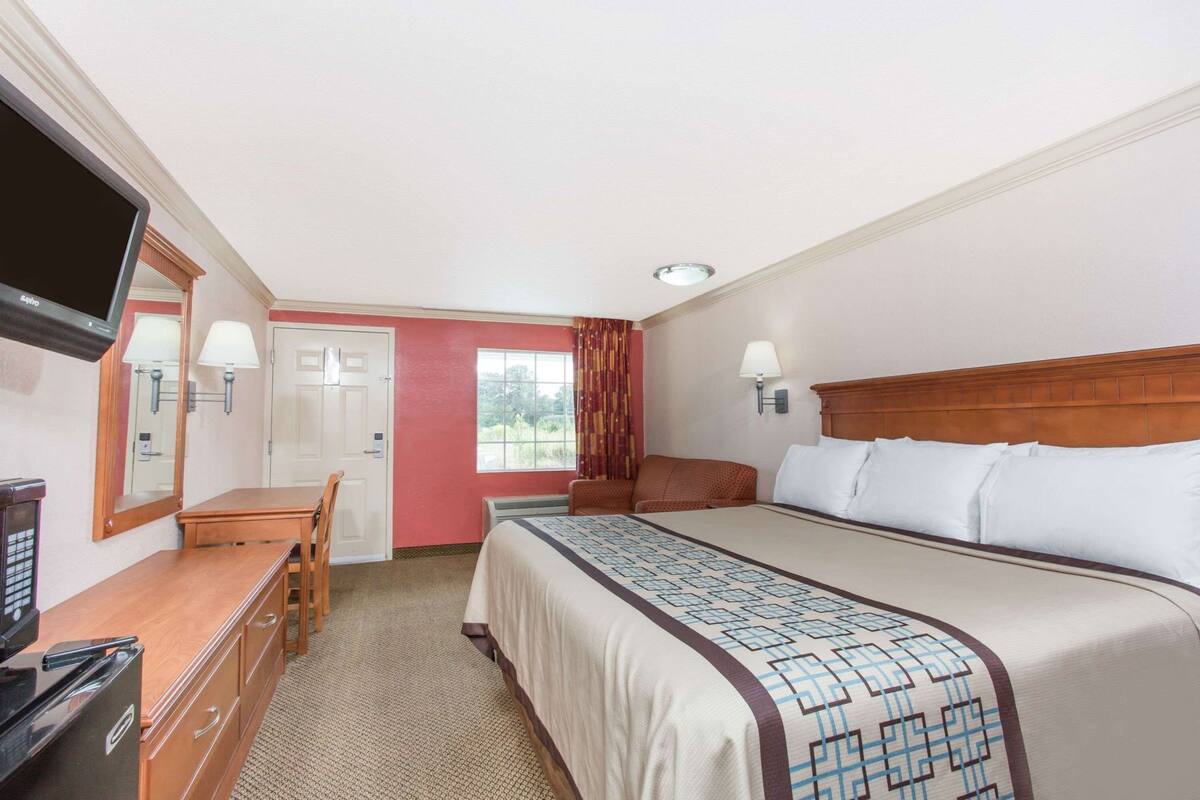 A hotel room with a bed, a desk, a television, and a window with curtains.