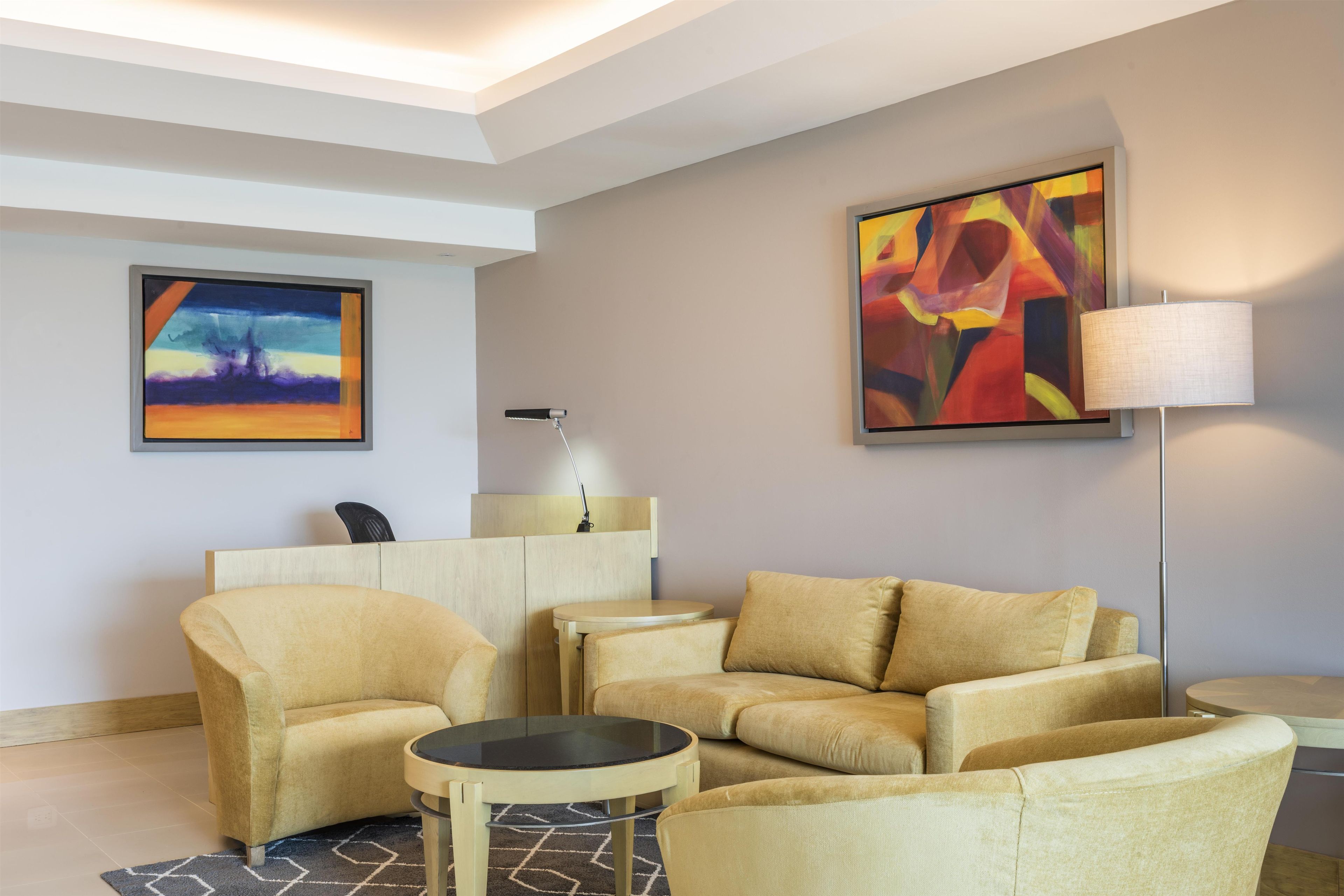 A modern living room with a sofa set, a small round table, a lamp, and two paintings on the wall.