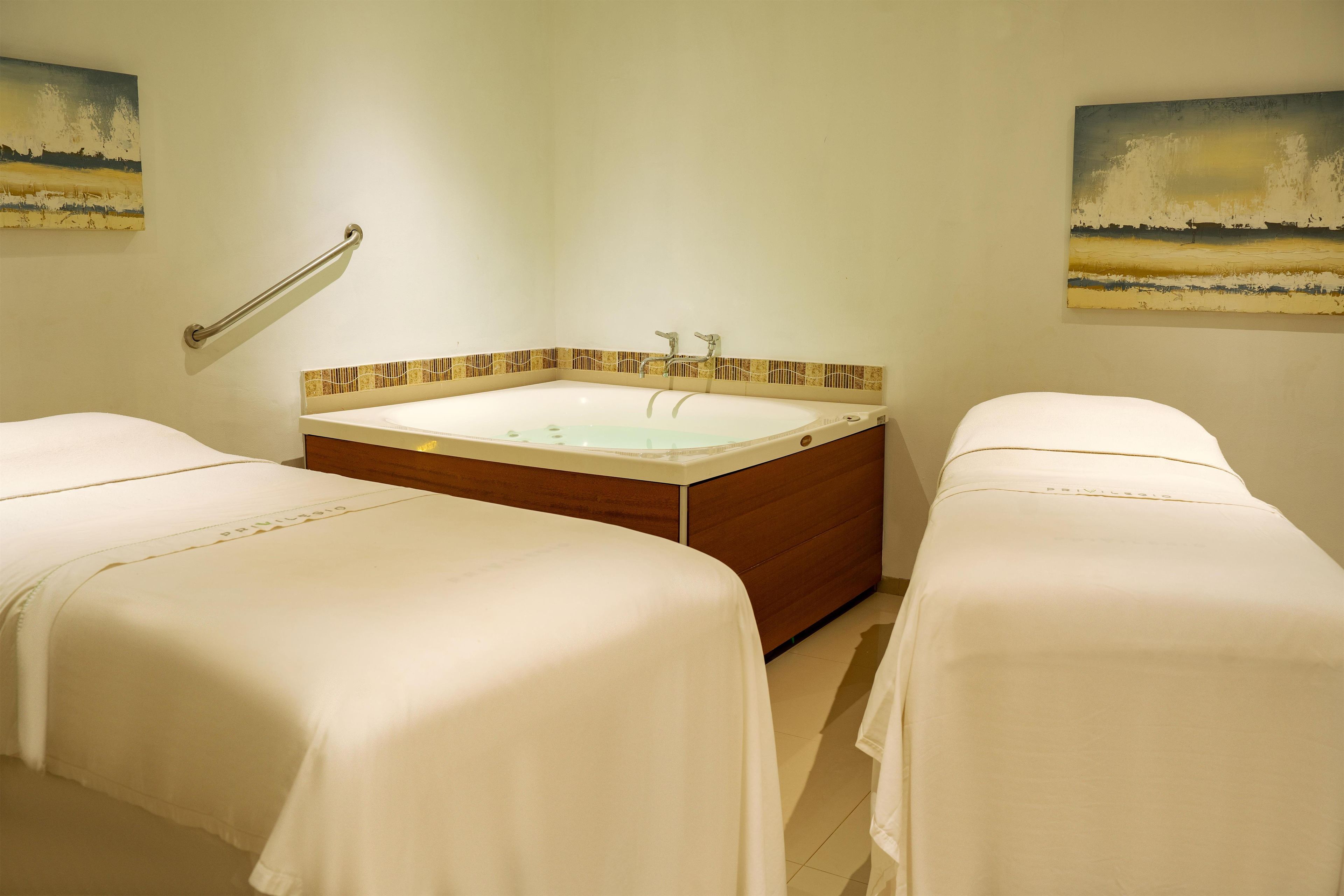 A room with two beds, a bathtub, and two paintings on the walls.