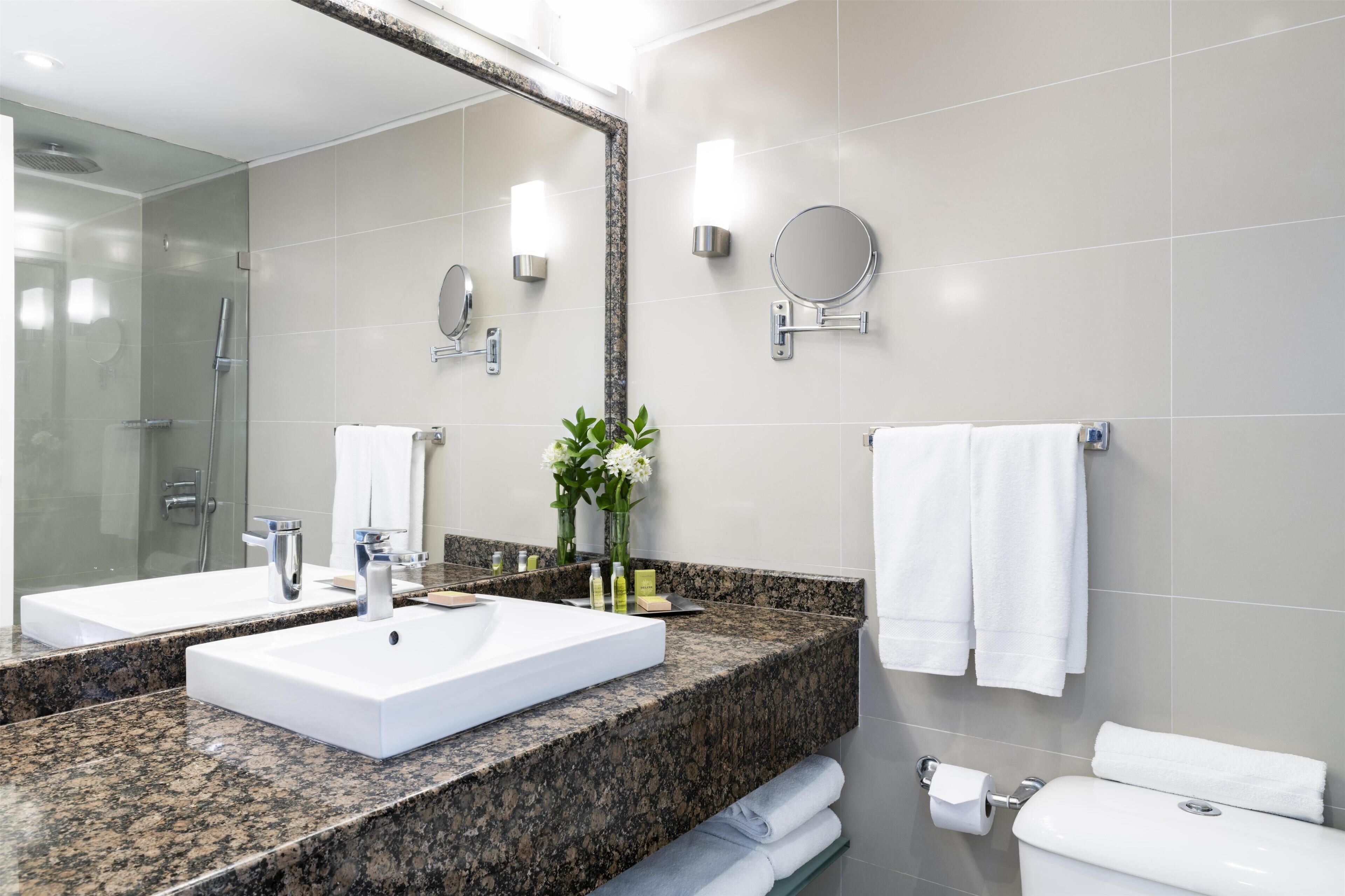 Un baño moderno con encimera de granito, dos lavamanos, un espejo grande y un inodoro.