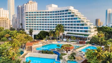 Un hotel con múltiples piscinas, un edificio amplio con muchas ventanas y vegetación circundante.