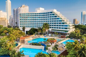 A hotel with multiple swimming pools, a large building with many windows, and surrounding greenery. - Hilton Cartagena (Cartagena)