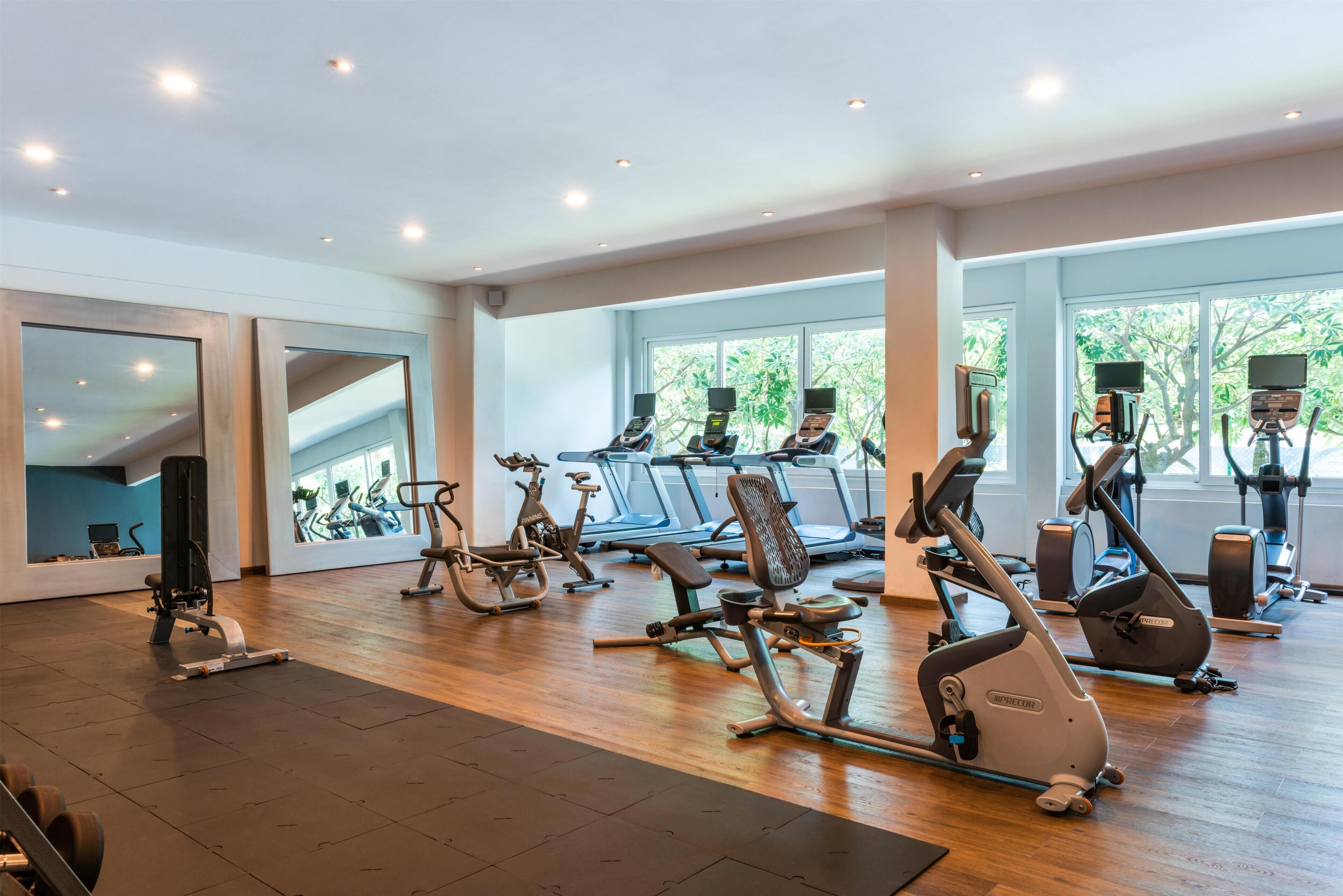 Un gimnasio con máquinas de cardio, espejos y amplias ventanas.