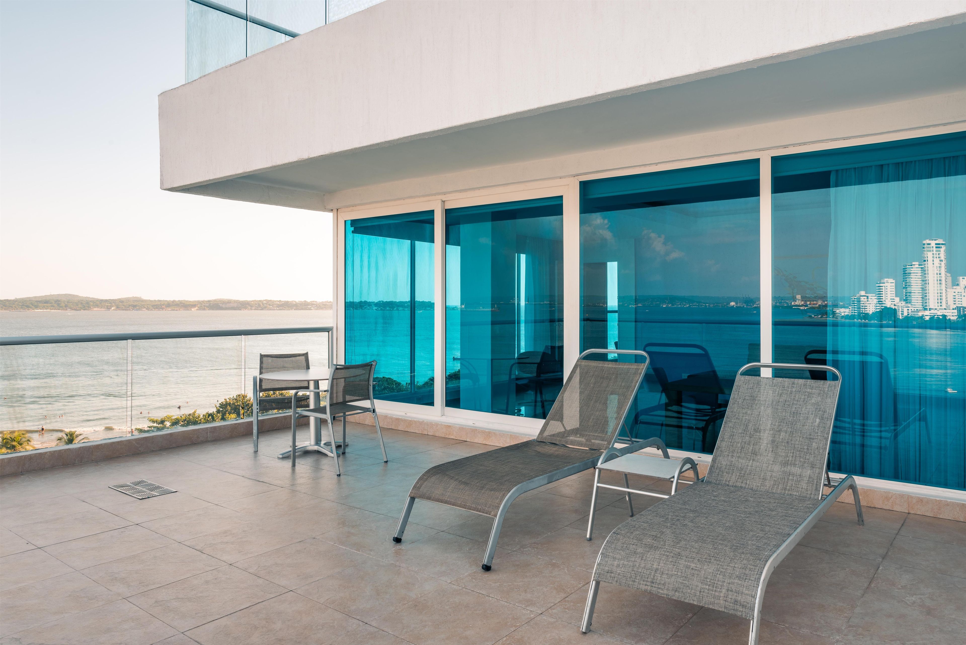 A balcony with a view of the sea, two lounge chairs, and a table.