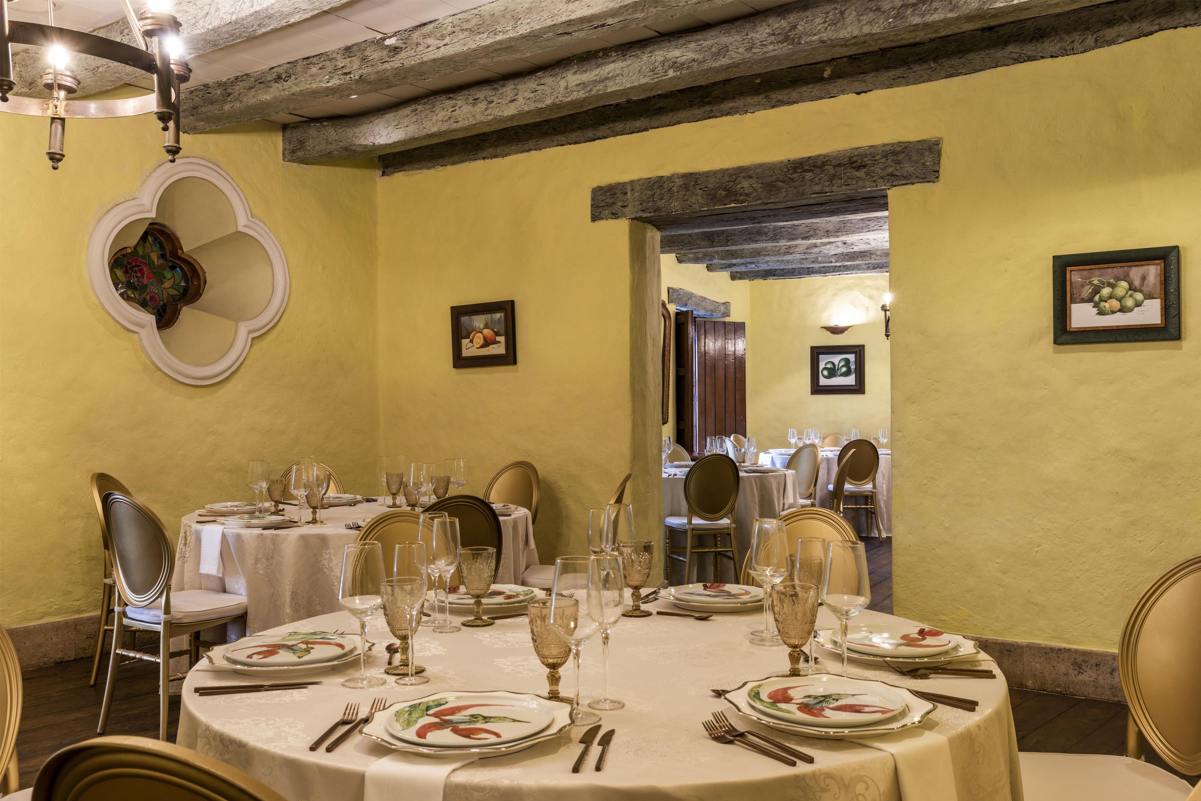 Un'area pranzo con tavoli rotondi apparecchiati per un pasto, con piatti decorati con motivi floreali, bicchieri da vino e posate.