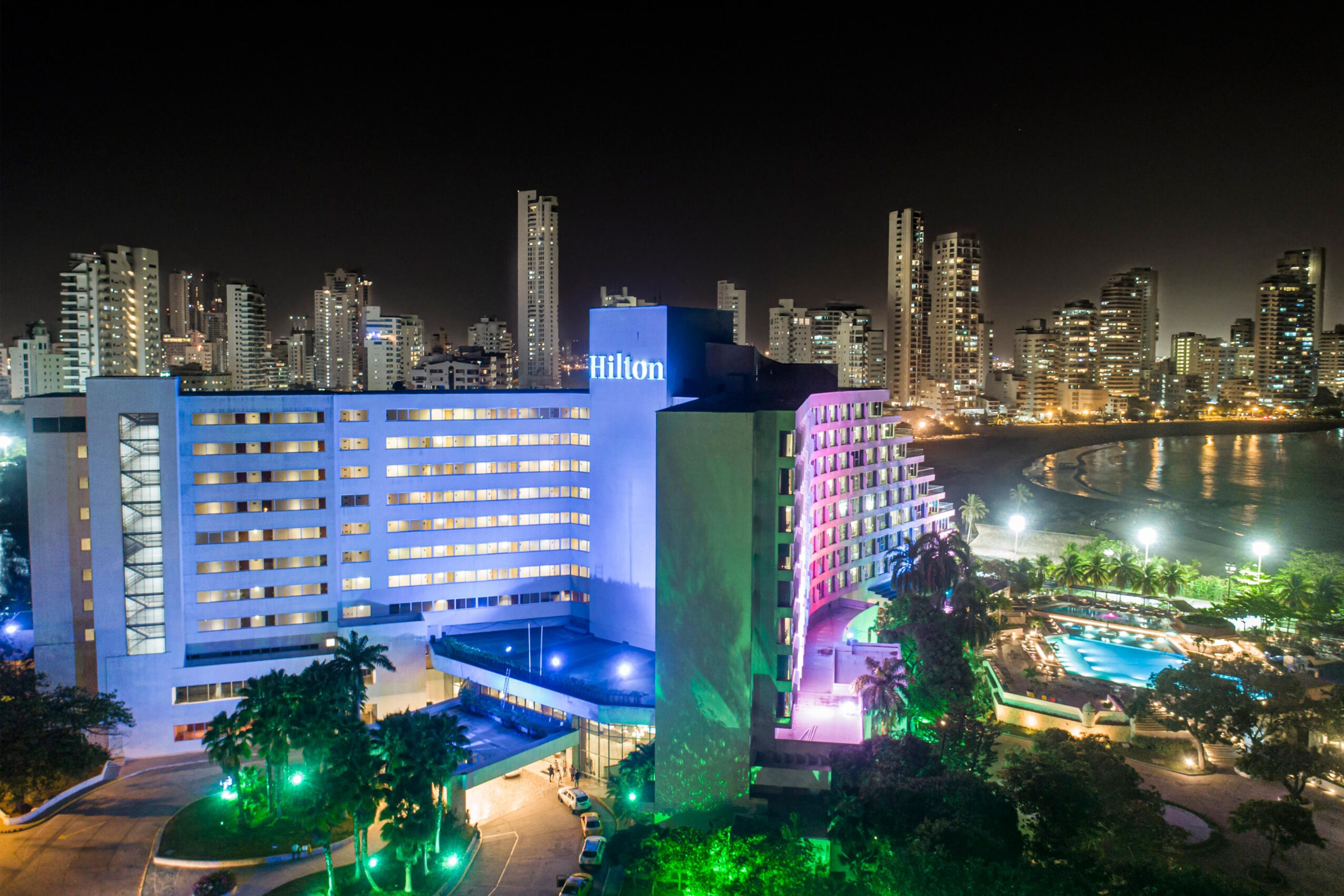 A hotel with a modern design, a pool area, and a view of the city skyline at night.