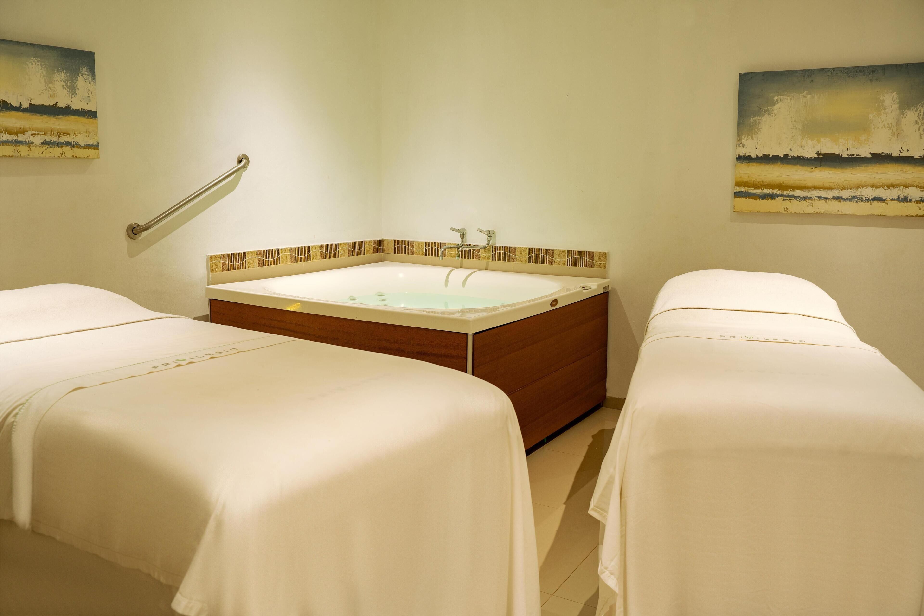A room with two beds, a bathtub, and artwork on the walls.