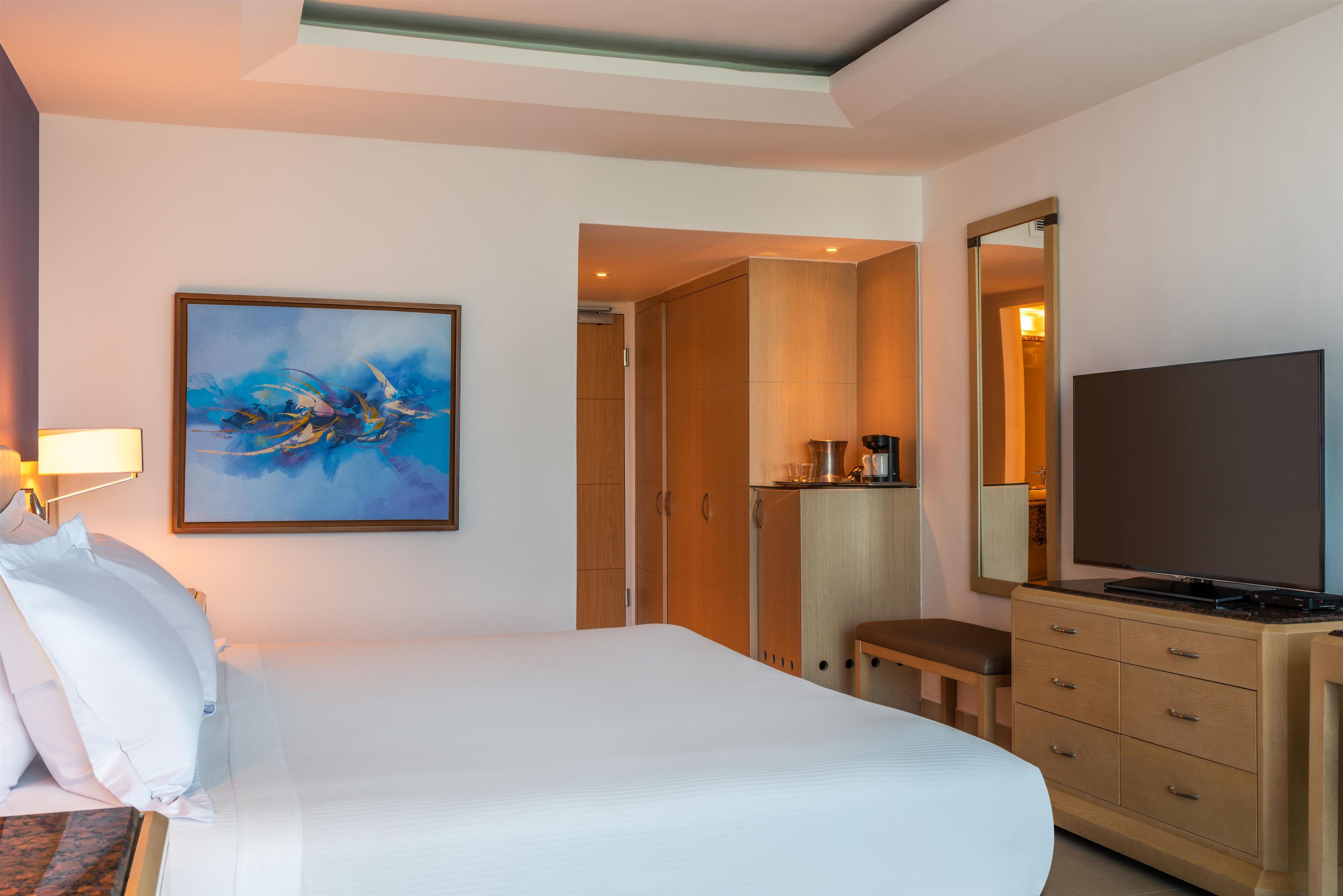 A hotel room with a bed, a painting, a television, and a wardrobe.