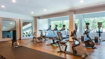 Ein Fitnessstudio mit verschiedenen Trainingsgeräten, großen Fenstern und einem Holzboden.