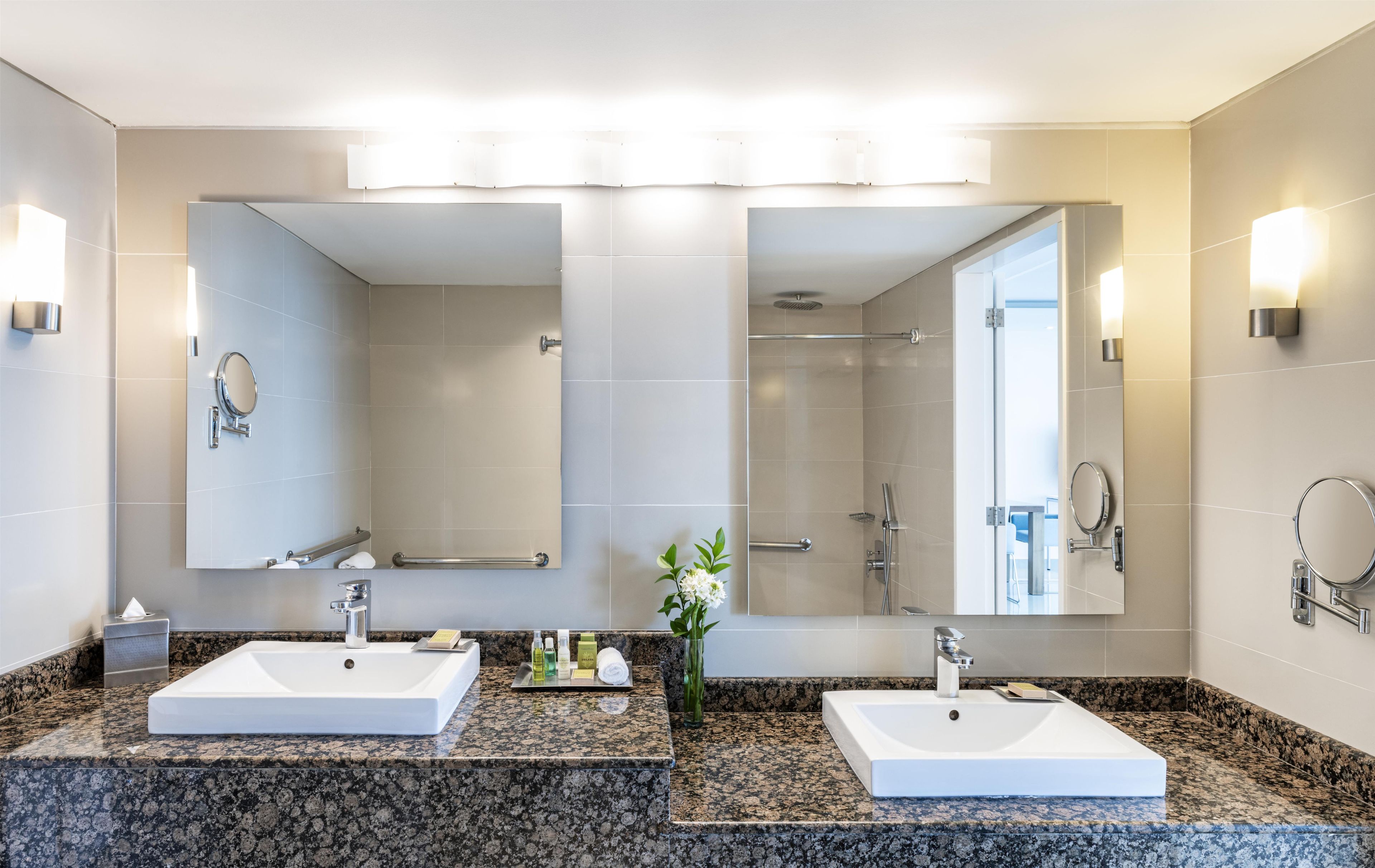 Une salle de bain moderne avec deux lavabos, une douche et un grand miroir.