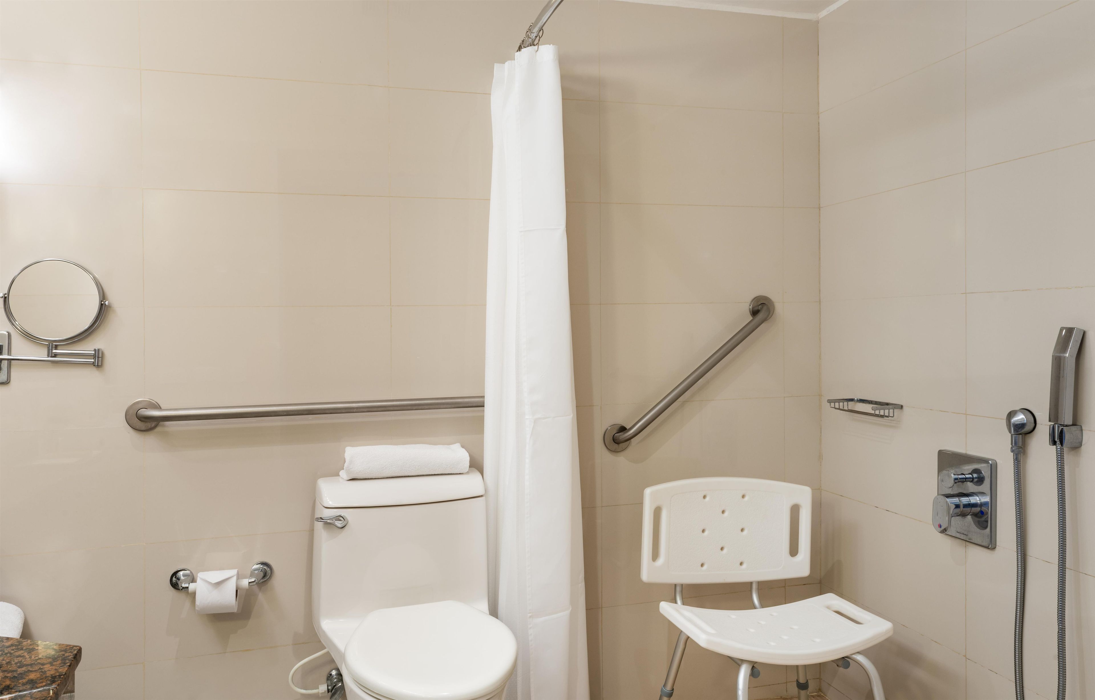 Une salle de bain équipée de toilettes, d’une douche, d’une barre d’appui, d’une serviette et d’un pommeau de douche amovible.