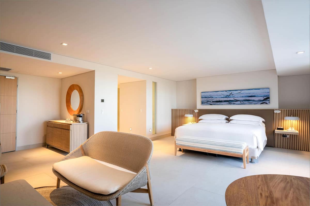 Et moderne hotelværelse med en seng, en stol, et natbord, en lampe og et billede på væggen.