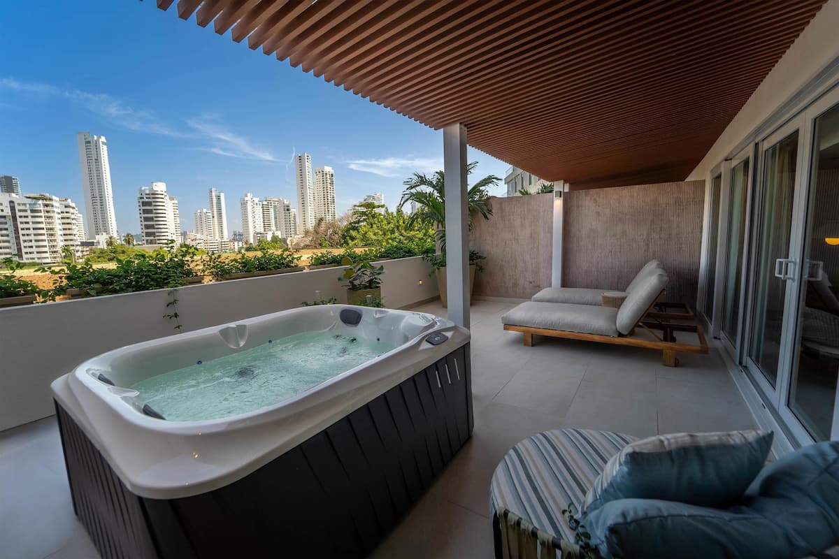 En balkon med jacuzzi, liggestol og udsigt til høje bygninger.