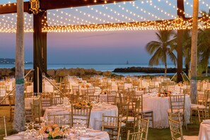 An outdoor banquet hall with round tables, gold chairs, and string lights. - Hilton Cartagena (Cartagena)