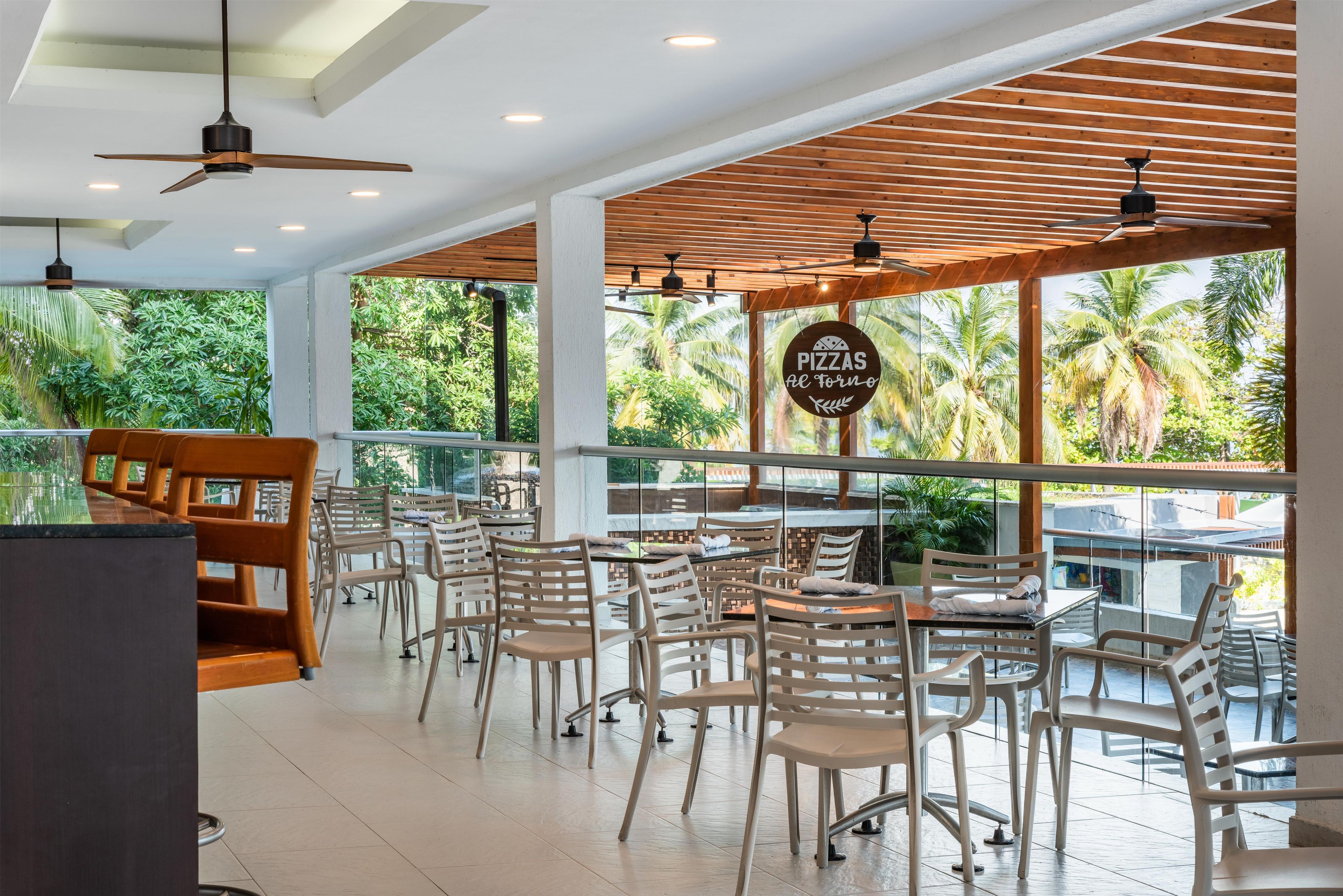 A restaurant with outdoor seating, large windows, and a sign for pizzas al forno.