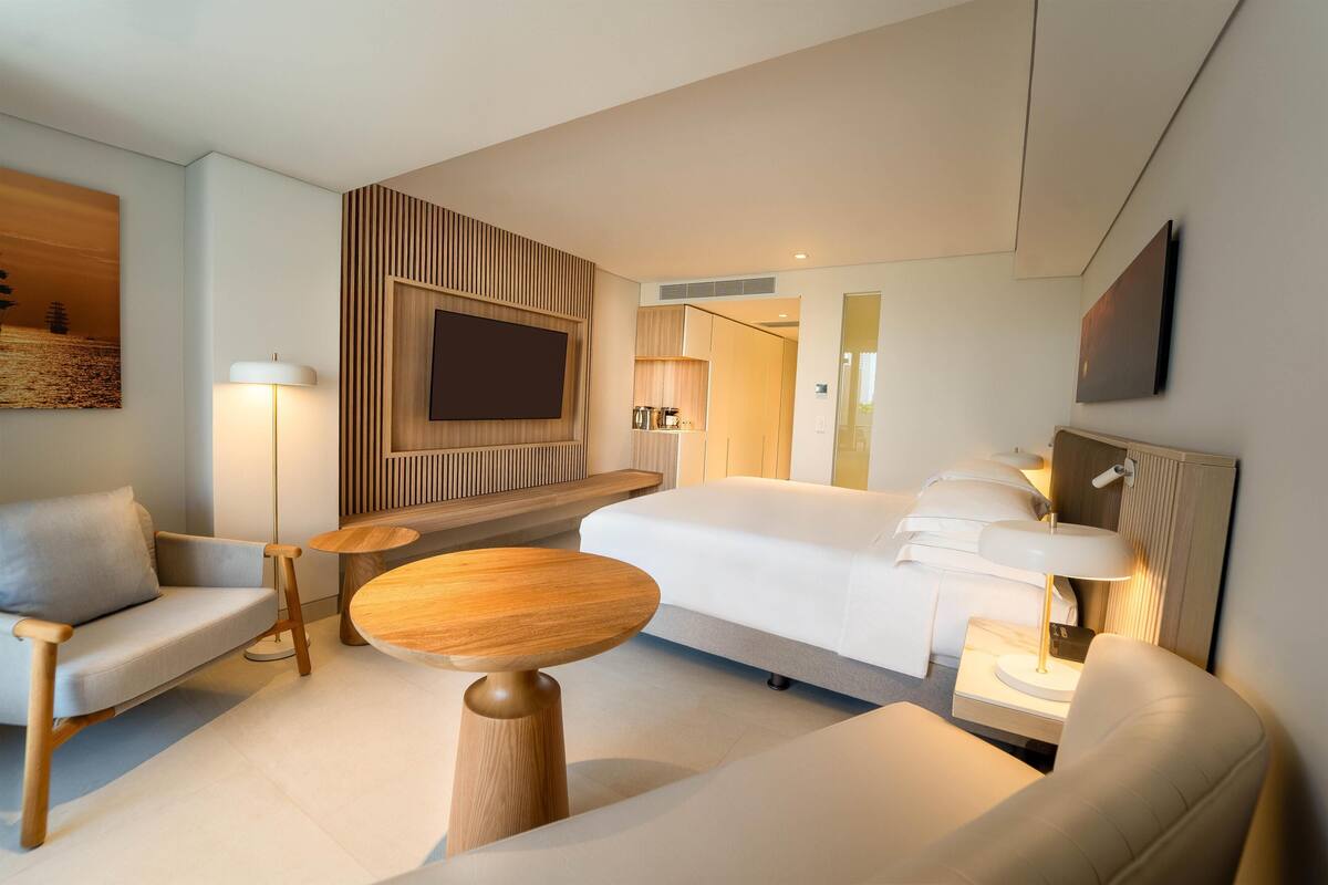 Et moderne hotelværelse med seng, sofa, rundt træbord og et tv ophængt på væggen.