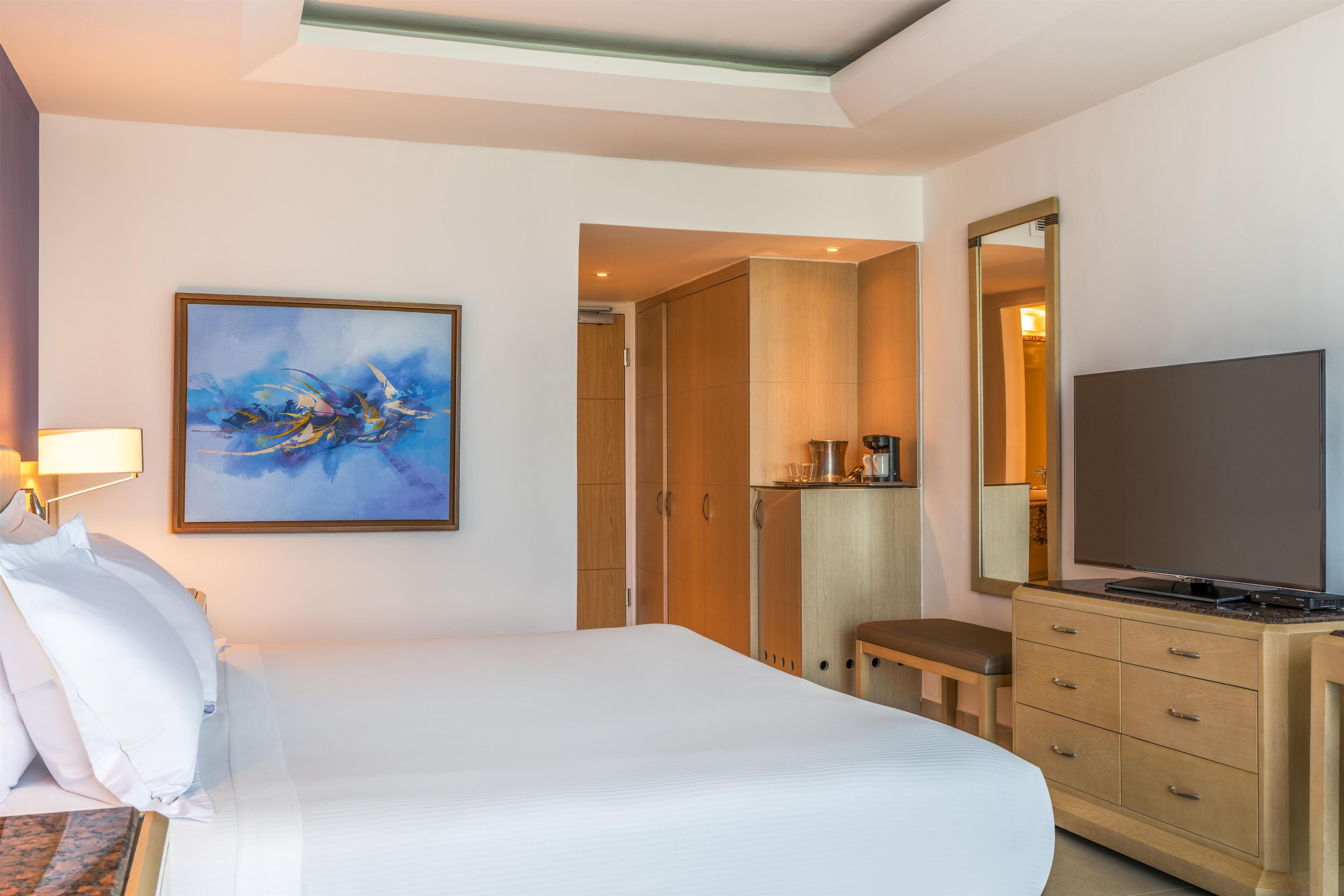 Una habitación de hotel con una cama, un cuadro, un televisor y una kitchenette.