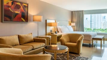 Habitación de hotel con cama, dos sofás, una mesita, una mesita de noche y un cuadro abstracto grande.