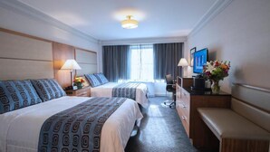 A hotel room with two beds, a desk, a chair, a TV, and a window with curtains. - Travel Inn Hotel (New York)