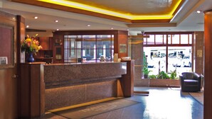 A reception area with a marble counter, a vase of flowers, and a view of the parking lot through glass doors. - Travel Inn Hotel (New York)