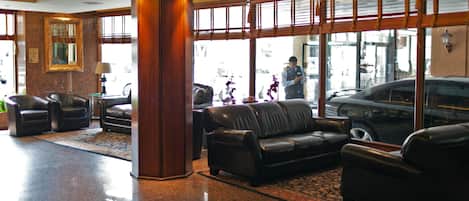A lobby with leather sofas, a large pillar, and a view of the street through large windows.