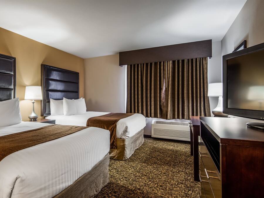 A hotel room with two beds, a TV, a desk, and a large window with curtains.