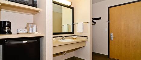 A hotel bathroom with a microwave, coffee maker, sink, and a large mirror.