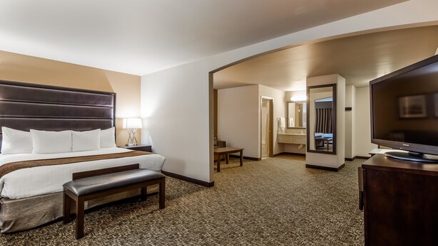 A hotel room with a large bed, a desk, a television, and a bathroom visible through an open door. - Best Western Oak Meadows Inn (St. Helens)
