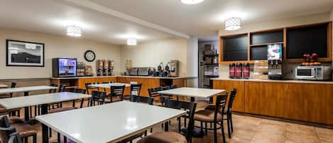 Un restaurante con varias mesas y sillas, una máquina de café, un microondas y una exhibición de frutas.